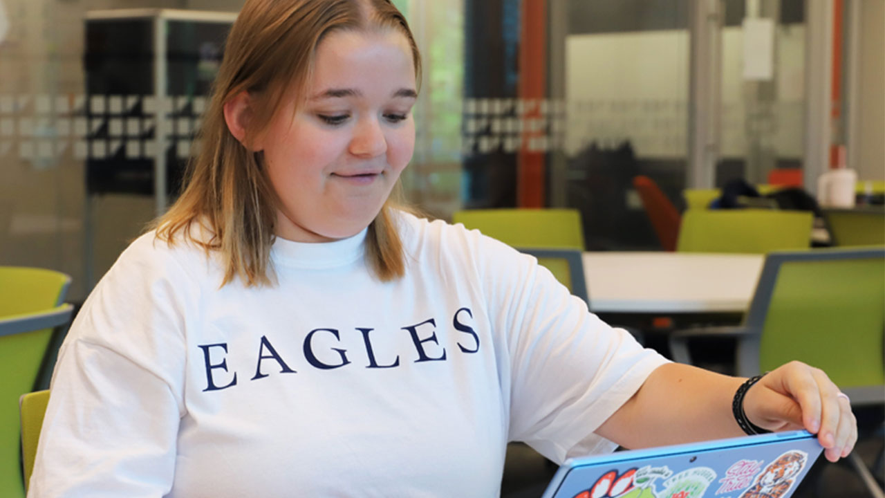 A student is pictured wearing an EAGLES shirt